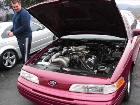 1992 Ford Crown Victoria - A maroon 1992 Ford Crown Victoria is shown with its hood open, revealing a modified engine with a turbocharger. Another vehicle is visible…
