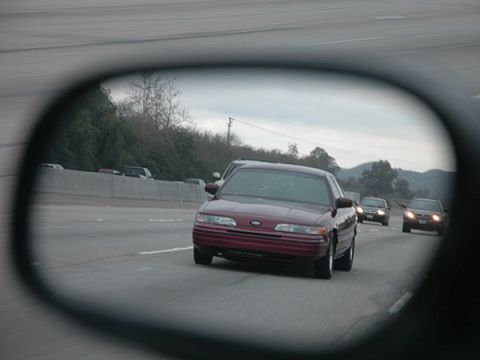 1992 Ford Crown Victoria - A red 1992 Ford Crown Victoria is seen in the side mirror while driving on the highway, with other vehicles visible ahead.