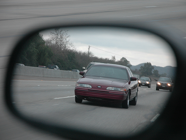 Red 1992 Ford Crown Victoria seen from side mirror on highway