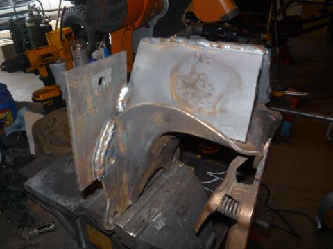 1979 Ford Bronco - A fabricated bare-steel bracket assembly clamped in a bench vise, built from a flat drilled plate MIG-welded to a curved arched section wit…