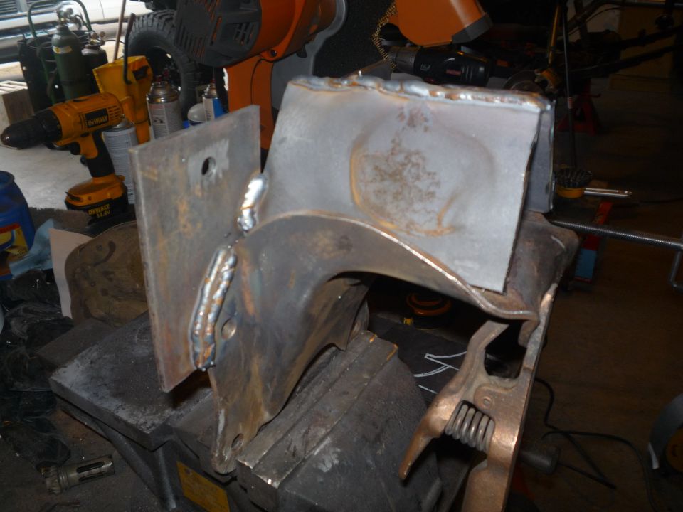 Welded bare-steel bracket with fresh MIG beads clamped in a bench vise in a garage