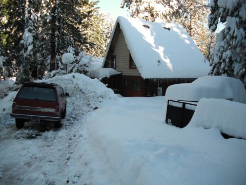 1991 Ford Bronco - A red SUV is parked in a driveway covered in deep snow, with a house and another snow-covered vehicle in the background.