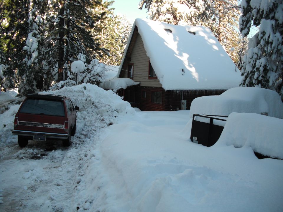 Red SUV parked in snow, rear view. Another vehicle covered in snow