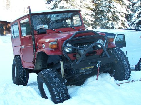 1990 Chevrolet Suburban - A red Toyota Land Cruiser FJ40 is stuck in the snow, partially obscured by a white van.