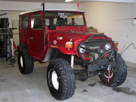 1990 Chevrolet Suburban - This red Toyota Land Cruiser FJ40 has a white roof and is equipped with large off-road tires.