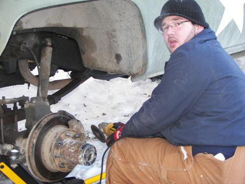 1990 Chevrolet Suburban - A person works on the suspension of a vehicle, with snow on the ground and a SuperMotors.net watermark visible.