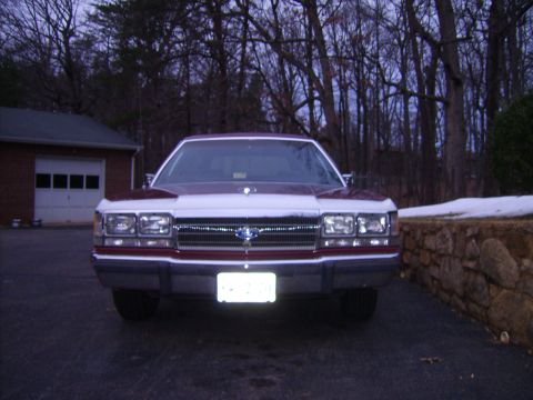 1988 Ford Crown Victoria LTD - The front end of a two-tone Ford Crown Victoria is shown parked outside a home with trees and snow in the background.