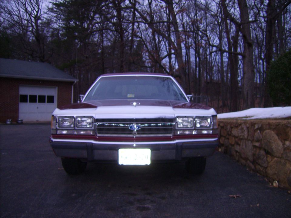 Front view of a maroon and white 1988 Ford Crown Victoria LTD parked in a driveway with a brick garage in the background