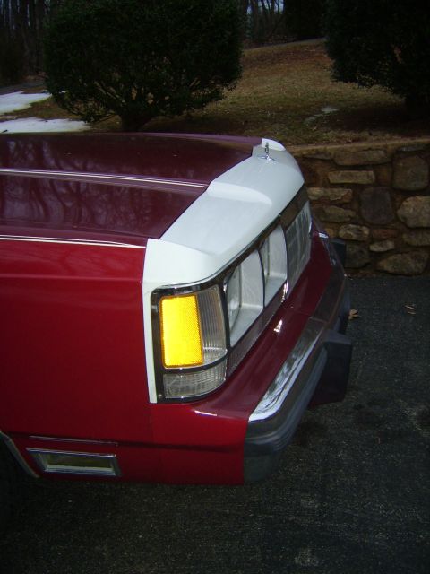 1988 Ford Crown Victoria LTD - The front corner of a red car shows a distinctive grille and headlight design.