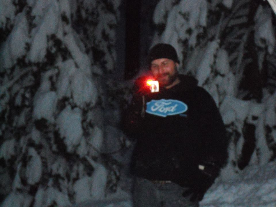 Man in black hoodie with Ford logo holds camera with red light in snowy woods