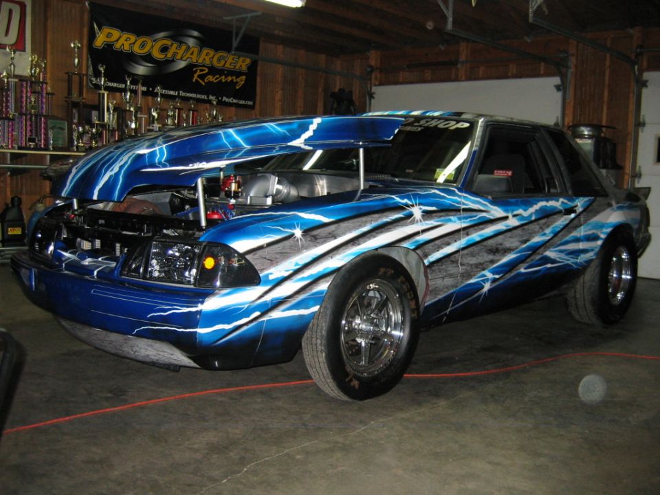 Blue Ford Mustang with lightning bolt graphics and exposed engine. Hood is open