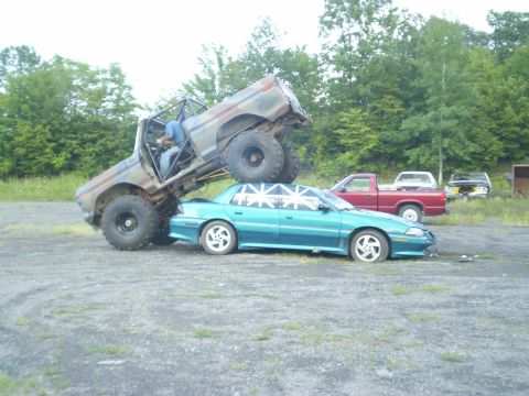 1979 Ford Bronco - A modified 1979 Ford Bronco monster truck is shown crushing a sedan, with other vehicles visible in the background.