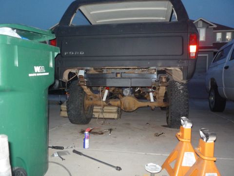 1979 Ford Bronco - Rear view of a black Ford Bronco with the tailgate lettering visible, jacked up in a driveway at dusk with its rear bumper removed to expos…