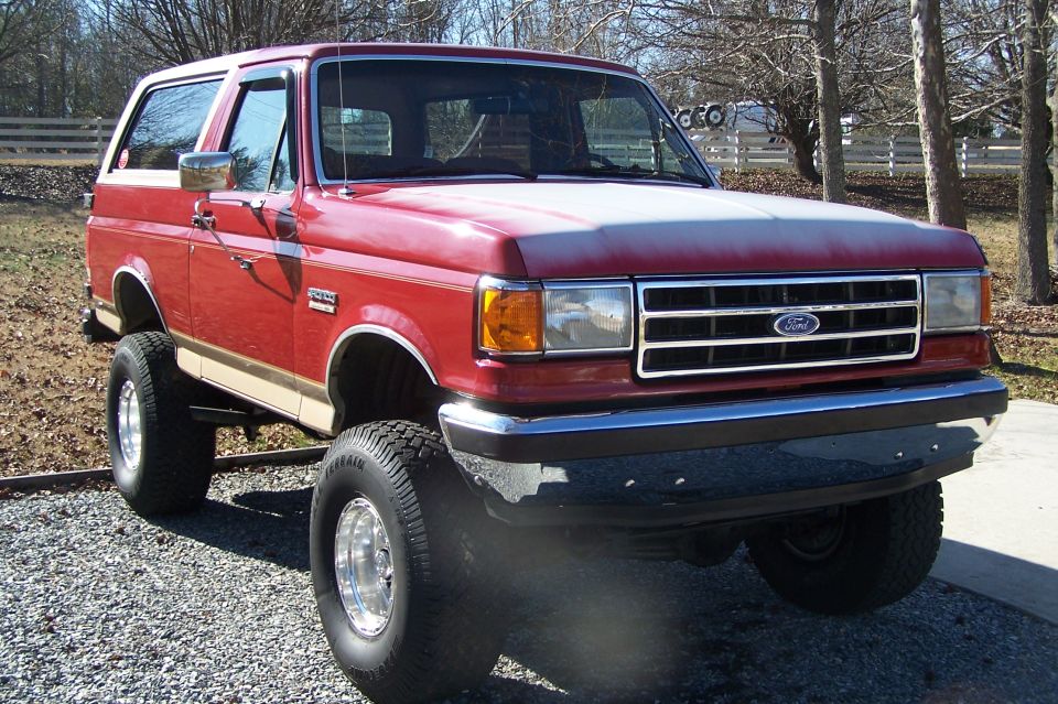 Front three-quarter view of a red lifted Ford Bronco on chrome wheels