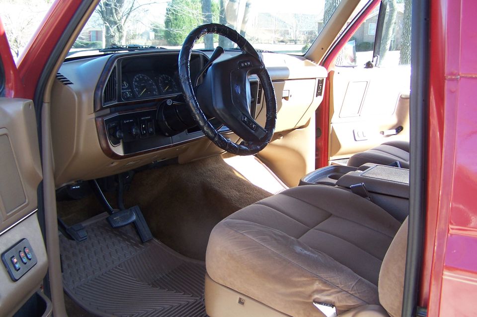 Tan interior of red Ford Bronco seen through open driver door, wrapped steering wheel and cloth seats