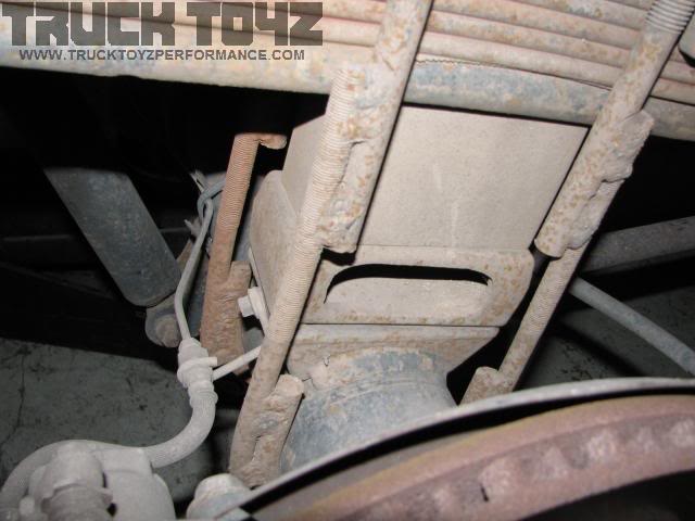 Muddy leaf spring pack and U-bolts clamped to a rear axle tube above the brake drum