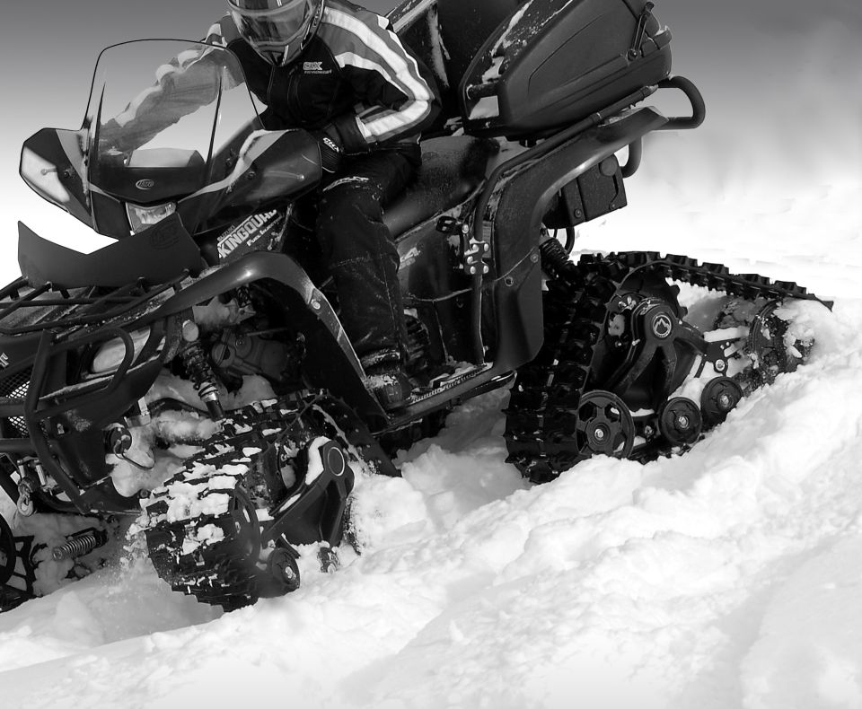 Track-converted ATV with rider driving through deep snow, black and white photo