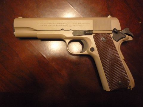 1979 Ford Bronco - A close-up view of a Colt 1911 pistol, showing its distinctive markings and textured grips.