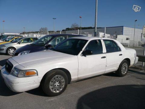 1991 Ford Crown Victoria - Side view of a white Ford Crown Victoria sedan parked outdoors with other vehicles.