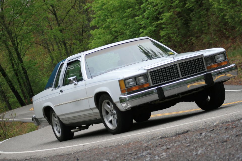 White 1980s Ford LTD Crown Victoria coupe cornering on a wooded road
