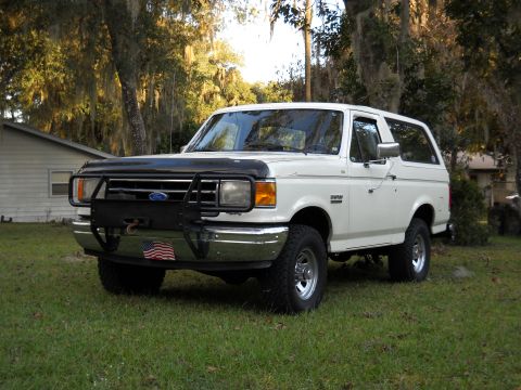 1989 Ford Bronco - A white Ford Bronco is parked on a grassy lawn in front of a house.