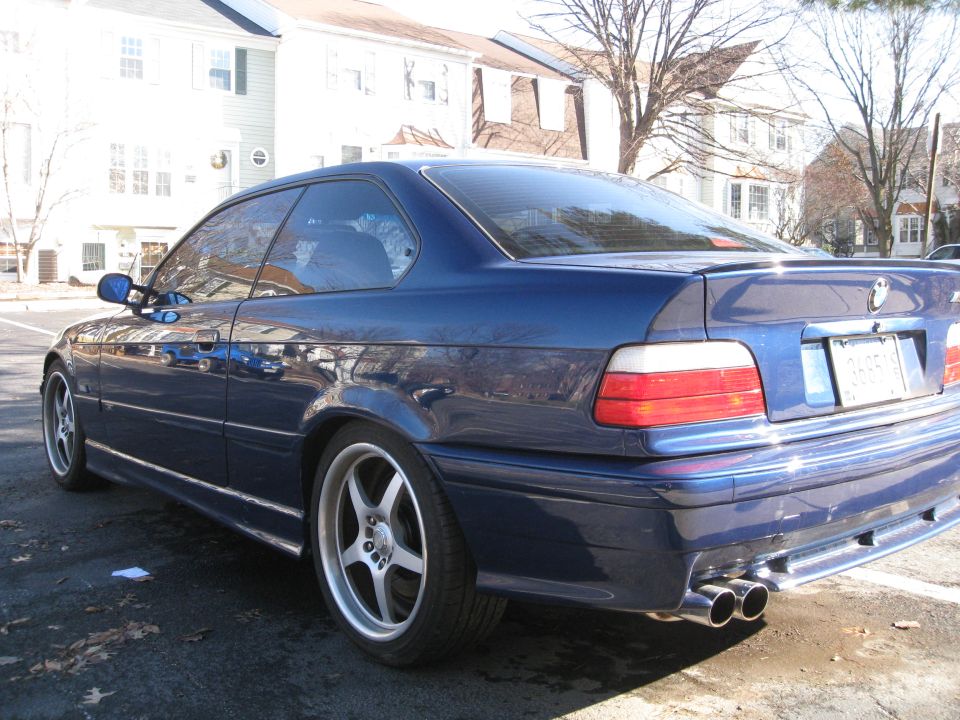 Blue coupe with aftermarket five-spoke wheels, dual exhaust, and a rear spoiler. The car is parked on asphalt