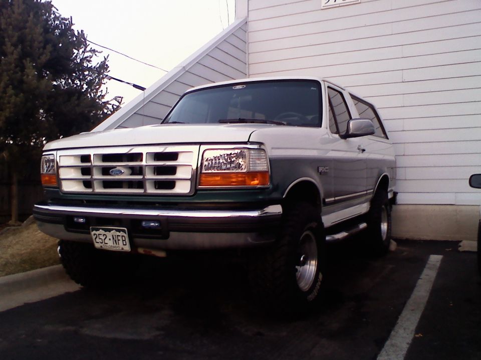 White and green Ford Bronco parked next to a building. License plate reads 252-NFB