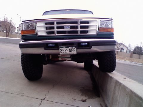 1996 Ford Bronco - Front view of a lifted Ford Bronco with a white grille and large tires, parked on a concrete curb.