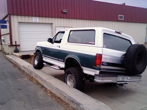 1996 Ford Bronco - This two-tone Ford Bronco is parked with its rear facing the camera, showing a spare tire mounted on the tailgate.