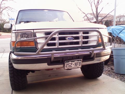 1996 Ford Bronco - Front view of a white and green two-tone 1990s Ford truck/SUV with a tubular gray brush guard over the chrome bumper and grille, sitting on…
