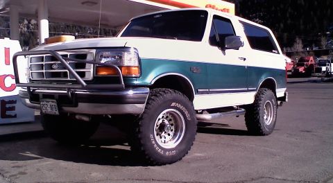 1996 Ford Bronco - This two-tone 1996 Ford Bronco features a prominent brush guard and lifted suspension, parked at a gas station.