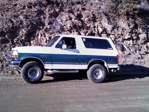 1996 Ford Bronco - This two-tone Ford Bronco is parked on a dirt road with a rocky hillside in the background.