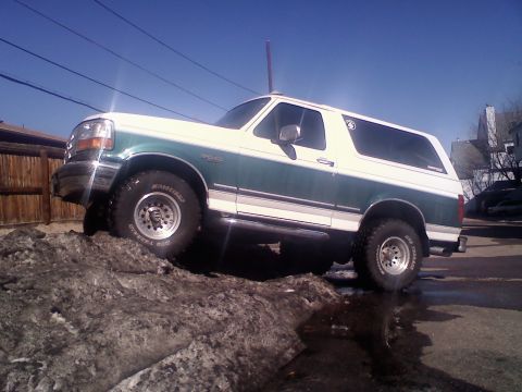 1996 Ford Bronco - Green-over-white two-tone Ford Bronco full-size SUV with removable hardtop, photographed from the driver's side as it climbs a dirty snowba…