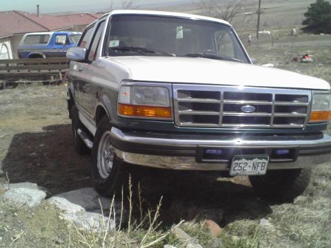 1996 Ford Bronco - Low three-quarter front view of a two-tone dark green and white Ford Bronco full-size SUV with a white removable hardtop, chrome grille wit…