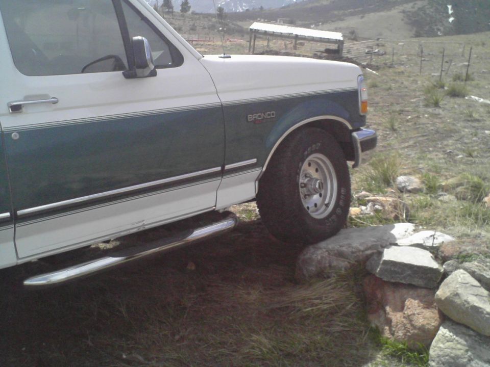 White and green 1996 Ford Bronco with chrome running boards on rocky terrain
