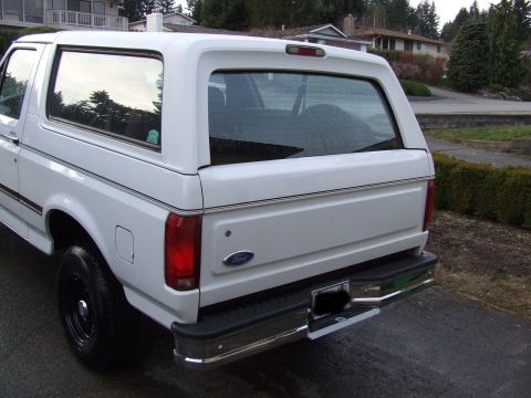 1996 Ford Bronco - This white Ford Bronco, viewed from the rear quarter, features a camper shell and chrome bumper.