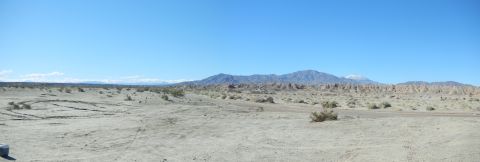1997 Ford Ranger - Wide desert panorama of an open sand wash with scattered creosote brush, tire tracks in the pale sand, eroded badlands and a snow-dusted mo…