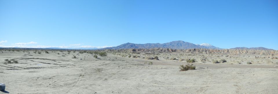 Panorama of open desert sand wash with tire tracks, badlands and distant mountains