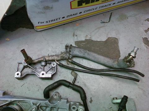 1992 Ford Bronco - A damaged engine part, possibly from a 1992 Ford Bronco, lies on a concrete surface with visible heat shielding and hoses.