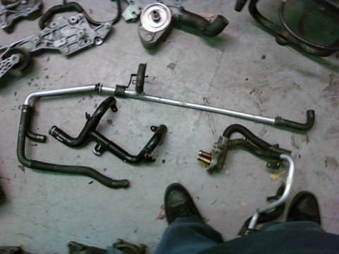 1992 Ford Bronco - Disassembled engine coolant lines and water pump assembly laid out on a concrete floor.
