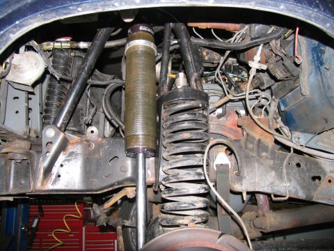 1984 Ford Bronco - Close-up view of the front suspension system, including coil springs and shock absorbers, on a blue vehicle.