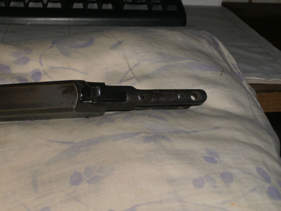 Dark metal firearm receiver stamped 'MODEL 37' on floral cloth