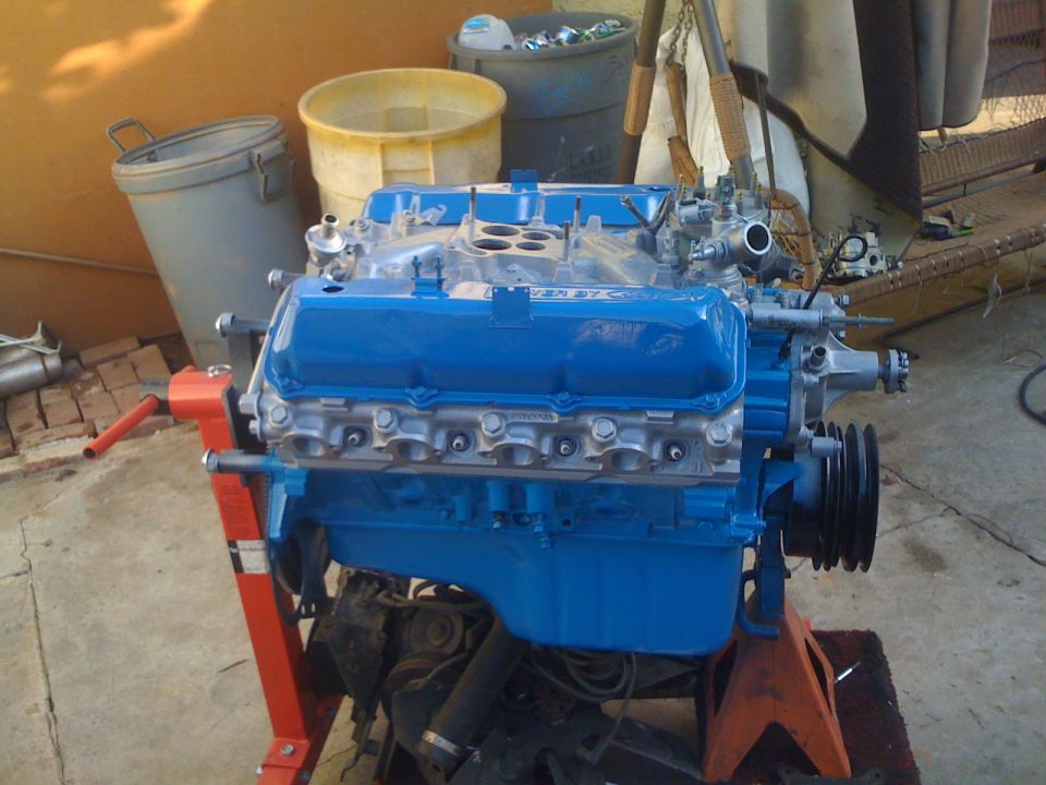 Blue V8 engine on an orange engine stand. It has blue valve covers with text on them