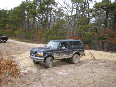 1994 Ford Bronco - A black 1994 Ford Bronco is seen off-road with another truck in the background.
