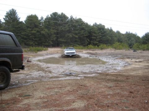 1994 Ford Bronco - Two Ford Broncos are present in a muddy outdoor scene with trees in the background.