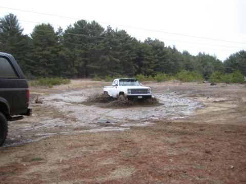 1994 Ford Bronco - White pickup truck driving through mud with a black SUV nearby.