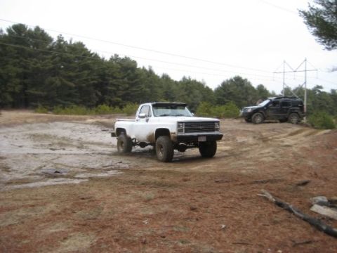 1994 Ford Bronco - A lifted white pickup truck navigates a muddy off-road course with another SUV in the background.