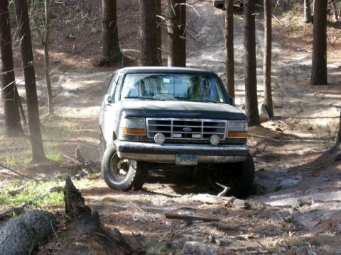 1994 Ford Bronco - Ford Bronco navigating a rough, wooded trail with its front wheels off the ground.