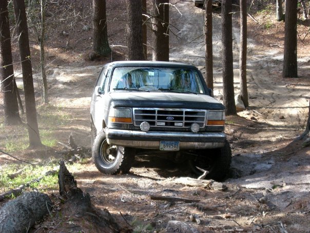1992 Ford Bronco driving on a wooded dirt trail, front view. License plate reads 694542