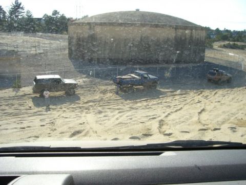 1994 Ford Bronco - Multiple off-road vehicles are seen in a sandy terrain near a large water tank.